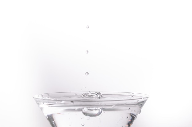 Close-up van waterdruppel die in een glas valt op witte achtergrond