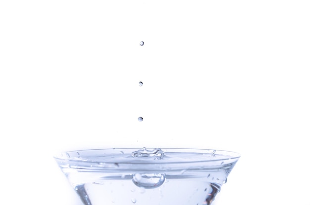 Close-up van waterdruppel vallen in een glas op witte achtergrond.