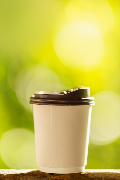 Close-up van wegwerpbare papieren kop warme koffie op houten balk met groene natuurachtergrond