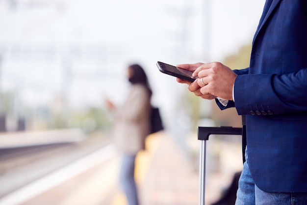 Close-up van zakenman op spoorwegplatform sms'en op mobiele telefoon