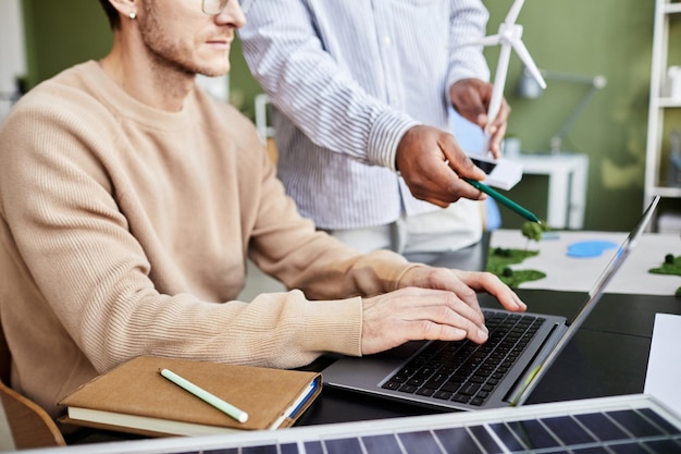 Close-up van zakenman zittend aan tafel en werken op laptop met zijn collega wijzend op monitor