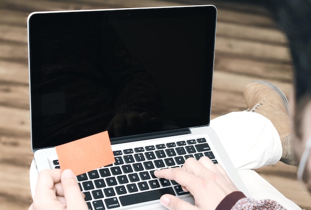 Close-up van zakenmanvingers op laptop terwijl hij papieren bonnetje bij de hand houdt