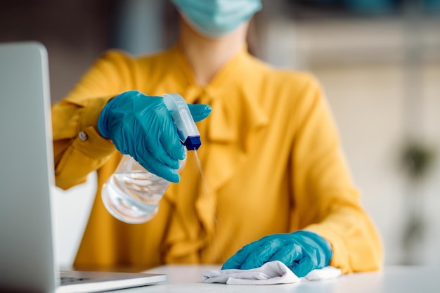 Close-up van zakenvrouw die haar bureau schoonmaakt met ontsmettingsmiddel