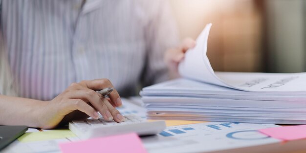 Close up van zakenvrouw of accountant hand met pen bezig met rekenmachine om zakelijke gegevens boekhouding document en laptopcomputer op kantoor bedrijfsconcept te berekenen