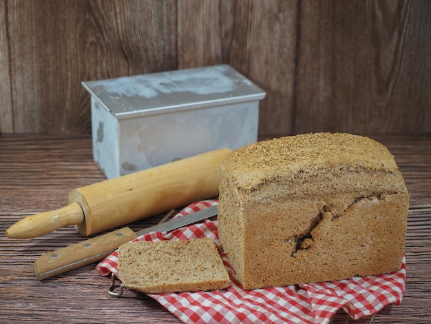 Foto close-up van zelfgebakken brood met bakkerijgerei op rood en wit geruit tafelkleed en houten achtergrond