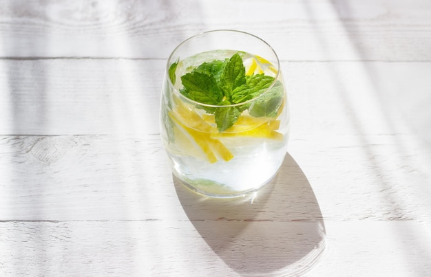 Close-up van zelfgemaakte limonade met citroenmunt en ijsblokjes in een glas op een witte houten achtergrond