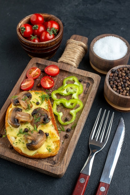 Close-up van zelfgemaakte smakelijke snack met champignons en gehakte groenten op houten bord bestek set kruiden op zwarte achtergrond