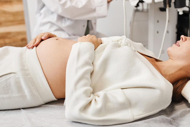Close up van zwangere jonge vrouw die zich voorbereidt op echografie in de medische kliniek met focus op buik