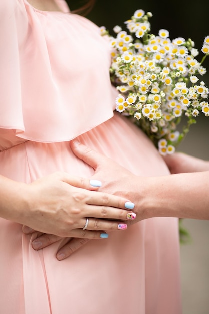 Close-up van zwangere vrouw met handen op haar buik op de achtergrond van de natuur Silhouet van zwangere vrouw in beige jurk Concept van zwangerschap moederschap familie verwachting voor baby geboorte Wachten op een kind