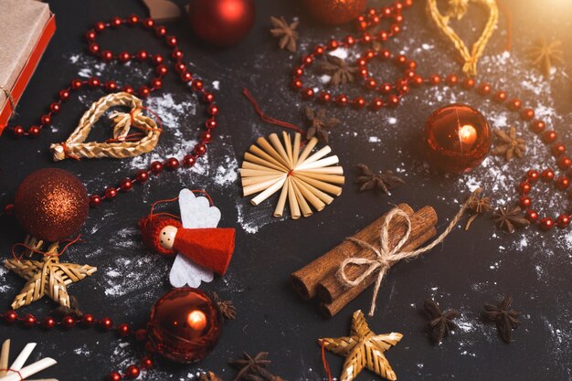 Photo close-up of various christmas toys, red balls, beads, cinnamon on black background