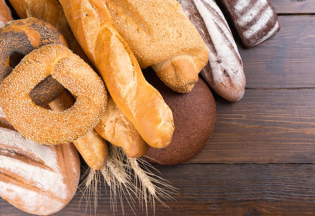 Close up of various types of whole baked bread loaves on mahogany wooden table with copy space