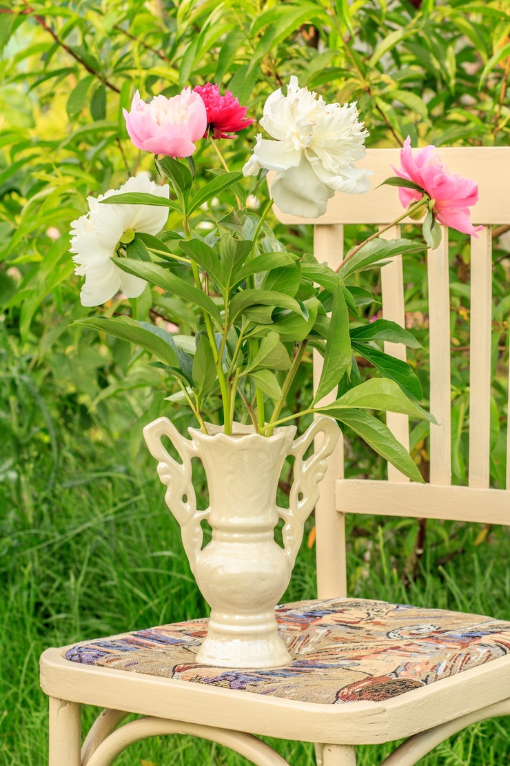 緑の自然の背景を持つ庭の白い素朴なスタイルの椅子に牡丹の花のクローズアップの花瓶。