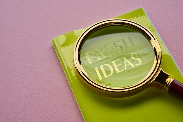 Close-up vergrootglas met tekst FRESH IDEAS op notitieblok tegen roze achtergrond