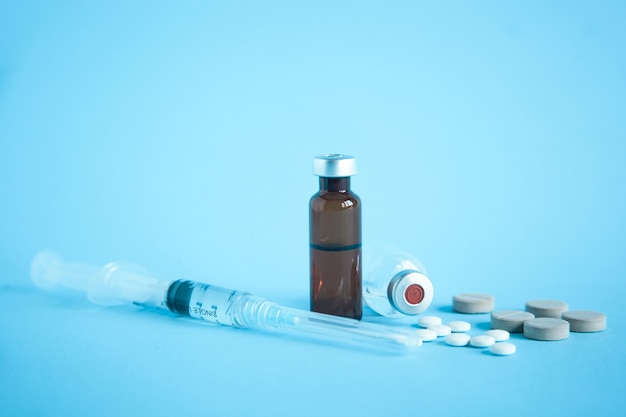 Close up of vial of medicine and vaccine with syringe and tablet on blue