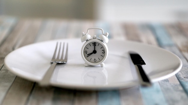 Vista ravvicinata dell'orologio sveglia su un piatto concetto di dieta a digiuno intermittente tempo per mangiare sano