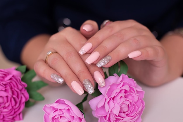 Close up view of beautiful female hands with romantic manicure nails, pink gel polish, peonies