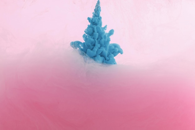 Крупный план брызг синей краски в воде, изолированной на розовом