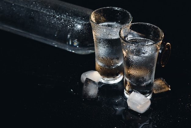 Vista ravvicinata di bottiglia e bicchieri di vodka in piedi isolato su nero