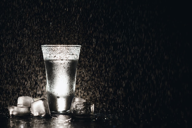 Close-up view of bottle of vodka with glasses standing on ice on black