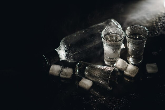 Close-up view of bottle of vodka with glasses standing on ice on black