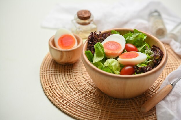 Close up view of a bowl of of salad with boiled eggs, lettuce and tomato on wicker placemat on the table