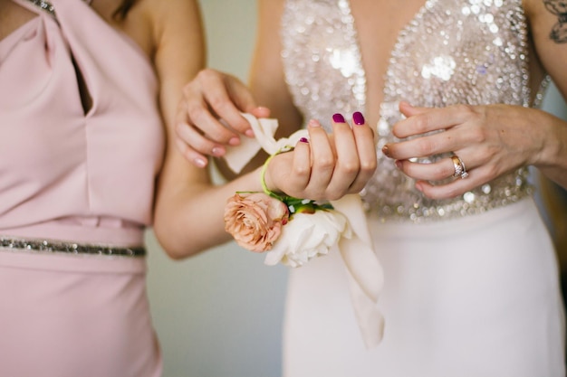 The close-up view of the brides hands tying the wedding wristband on the hand of the bridesmaid.