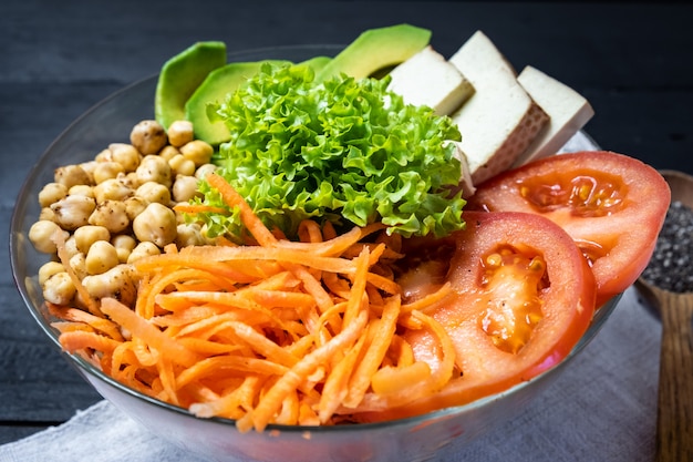 Close-up view of buddha bowl on a rustic table. Vegan meal of chickpeas, salad, vegetables, tofu and avocado