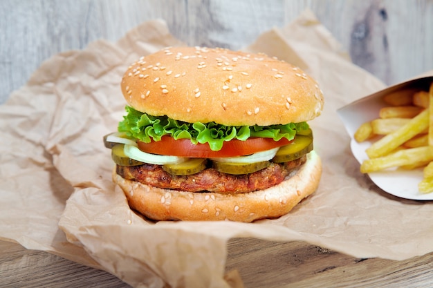 Close up view on burger with french fries on craft brown paper. Traditional fast food. fresh tasty hamburger with lettuce, tomato, cheese and cucumber. Copy space for design. Unhealthy food. Fat