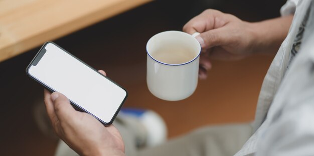 コーヒーを飲みながら空白の画面のスマートフォンを保持している実業家のクローズアップビュー