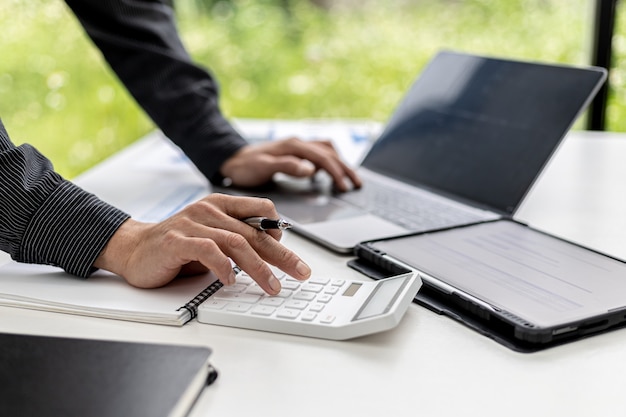 Close-up view A businessman using a calculator to calculate numbers on a company's financial documents, he is analyzing historical financial data to plan how to grow the company. Financial concept.