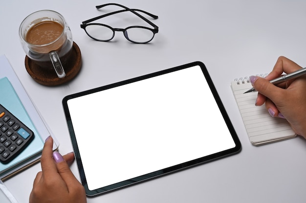 Vista ravvicinata imprenditrice utilizzando tablet digitale e scrivere informazioni sul notebook.