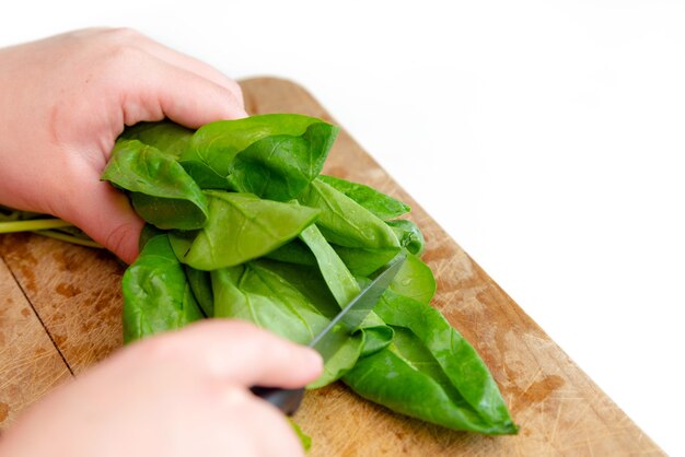 Close up view of chef hands cutting green spinach on wooden cutting board.