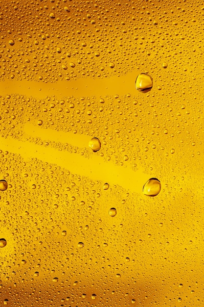 Close up view of cold drops on the glass of beer background. Texture of cooling alcohol drink with macro bubbles on the glass wall. Fizzing or floating up to top of surface. Golden colored.