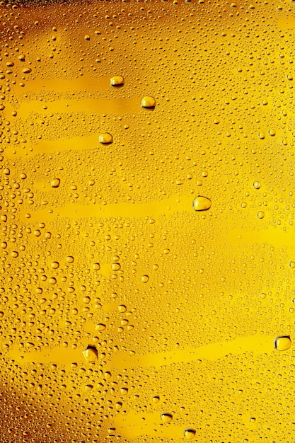 Close up view of cold drops on the glass of beer background. Texture of cooling alcohol drink with macro bubbles on the glass wall. Fizzing or floating up to top of surface. Golden colored.