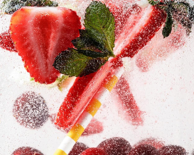 Close up view of cold and fresh lemonade with strawberry, cherry, mint leaves and ice cubes. texture of cooling summer's drink with macro bubbles on glass. fizzing or floating up to top of surface