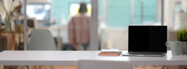 Close up view of comfortable office desk with open laptop, mug, tree pot, notebooks and copy space