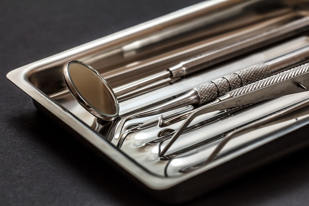 Close-up view of composite filling instruments for dental treatment. Medical tools in stainless steel tray on black background. Shallow depth of field. Focus on a mirror.