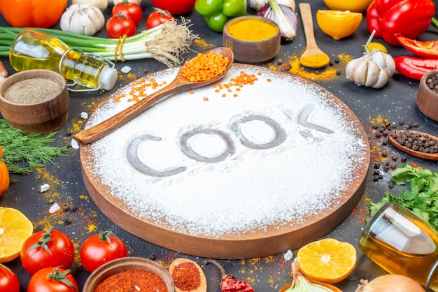 Close up view of cook writing with flour on wooden board among fresh vegetables spices green bundles fallen oil bottle on black surface