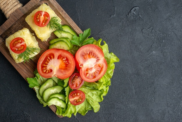 Close up view of cut fresh tomatoes and cucumbers on wooden board on black surface