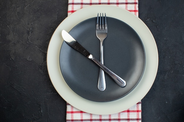 Close up view of cutlery set on dark gray color and white empty plates on red stripped towel on black background with free space