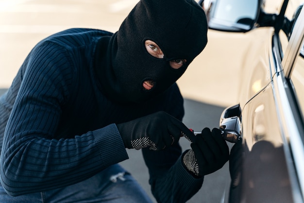 검은 옷을 입고 머리에 발라클라바를 얹은 위험한 남자의 가까이서 보면 훔치는 동안 곡괭이로 자물쇠를 따는다. 자동차 도둑, 자동차 절도 개념