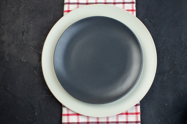 Close up view of dark gray color and white empty plates on red stripped towel on black background with free space