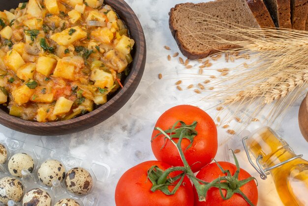 Close up view of delicious dinner with potatoes green in a brown bowl and bread slices tomatoes with stems fallen oil bottle pepper eggs on ice background