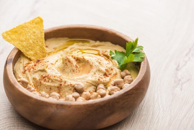 Close up view of delicious hummus with chickpeas and nacho in bowl on beige wooden table