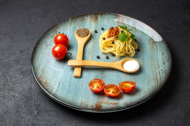 黒の背景のプレートにミートグリーントマトと一緒に出されるおいしいパスタの食事のクローズアップビュー