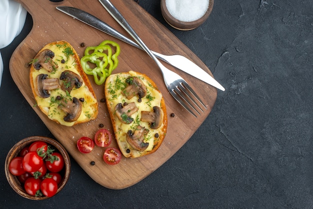 Крупным планом вид вкусных закусок с грибными свежими овощами и столовыми приборами на деревянной разделочной доске, белое полотенце, специи на черном фоне