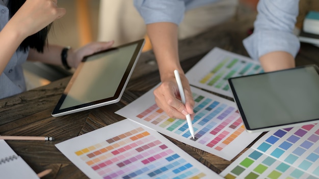 Close up view of designer team using digital tablet while choosing colour on colour swatch on vintage wooden table