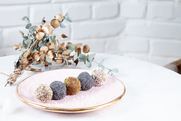 Close up view on different set of raw, healthy, no sugar, vegan candy. Sweet cakes for dieting menu. Gluten free sweets. Raw candy balls. Energy ball cakes on pink plate. Flat lay