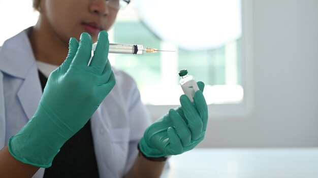 Close up view of doctor hand wears medical glove holding syringe and vaccine bottle.