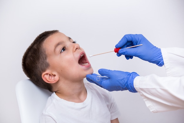 Close-up view doctor hands in gloves using cotton swab to test young boy for bacterial infections.